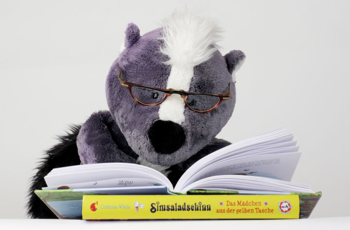 Das Plüschstinktier Teo liest in einem Kinderbuch von Corinna Wieja.